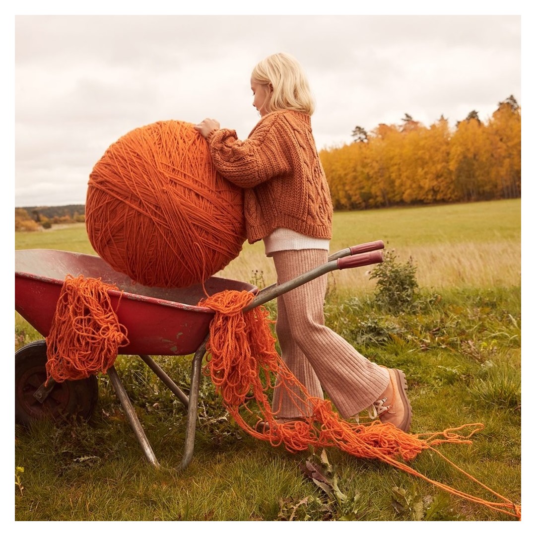 enfant mettant une énorme pelote de laine orange dans une brouette